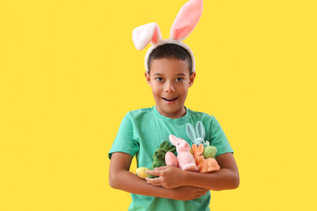 Little African-American boy with Easter eggs and rabbits on yellow background
