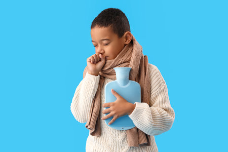 Ill African-American boy with hot water bottle coughing on blue backgroundの写真素材