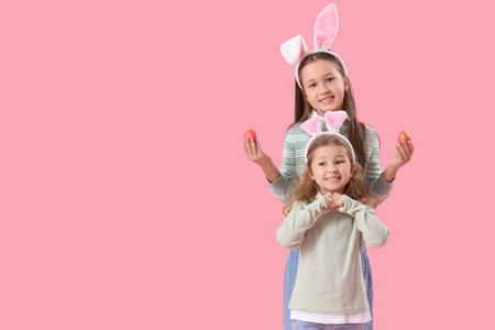 Little girls in bunny ears with Easter eggs on pink background