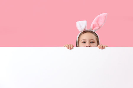 Little girl in bunny ears with blank poster on pink background. easter celebrationの写真素材