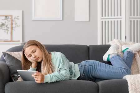 Little girl in earphones with tablet computer sleeping on sofa at homeの写真素材