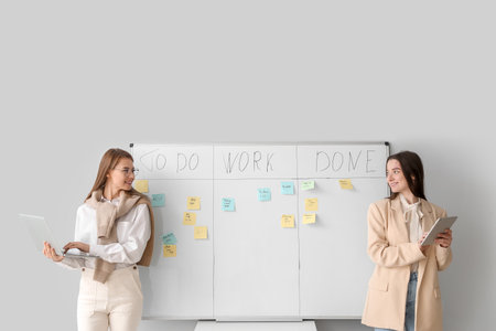 Young women with laptop and tablet computer near scrum task board in officeの写真素材