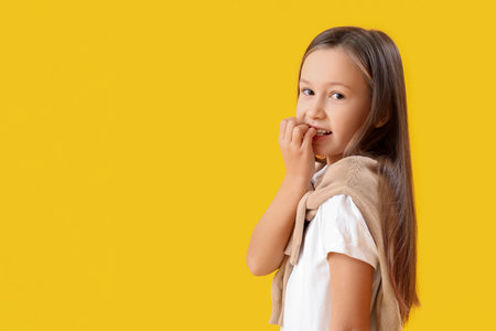 Little girl biting nails on yellow backgroundの写真素材