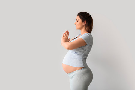 Young pregnant woman practicing yoga near light wallの写真素材