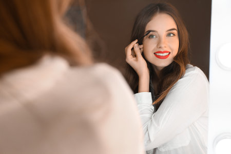 Young woman doing makeup near mirror in dressing roomの写真素材