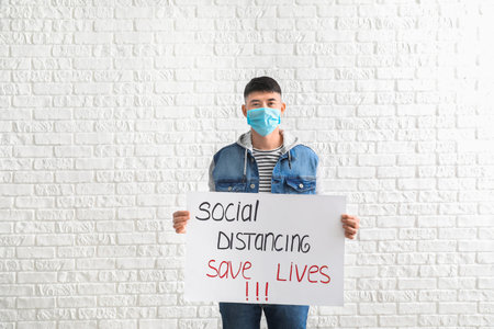 Young man holding paper with text SOCIAL DISTANCE. SAVE LIVES on white background. concept of...