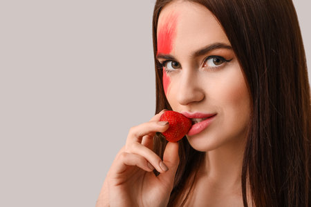 Sexy young woman with strawberry on light backgroundの写真素材