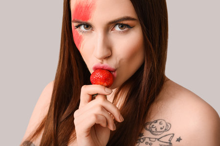 Sexy young woman with strawberry on light backgroundの写真素材