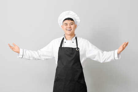 Handsome Asian chef showing something on gray backgroundの写真素材