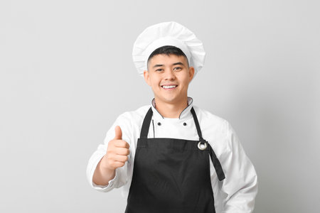 Handsome Asian chef showing thumb-up gesture on gray backgroundの写真素材