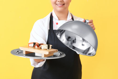 Beautiful Asian chef with sushi rolls on color backgroundの写真素材