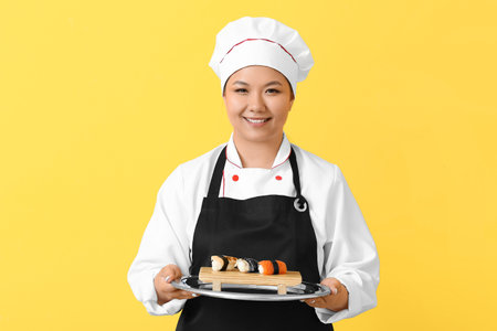 Beautiful Asian chef with sushi rolls on color backgroundの写真素材
