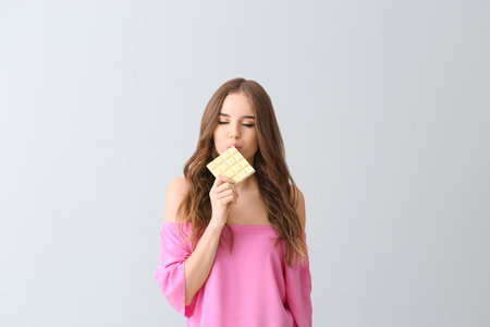 Beautiful young woman with tasty chocolate on light backgroundの写真素材