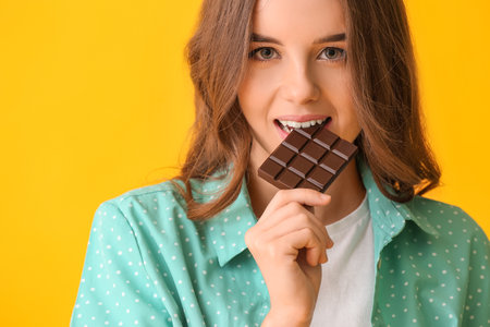 Beautiful young woman with tasty chocolate on color backgroundの写真素材