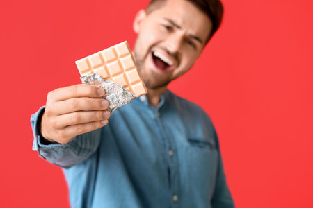 Handsome young man with tasty chocolate on color backgroundの写真素材