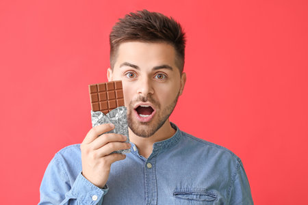 Surprised young man with tasty chocolate on color backgroundの写真素材