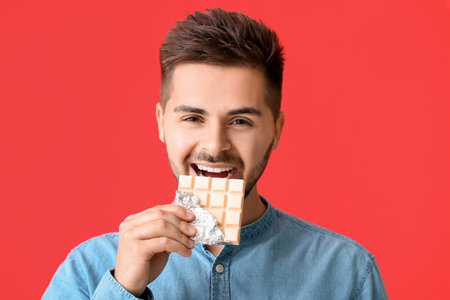 Handsome young man with tasty chocolate on color backgroundの写真素材