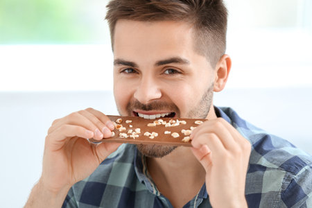 Handsome young man with tasty chocolate at homeの写真素材