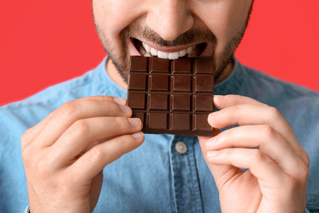 Handsome young man with tasty chocolate on color background, closeup