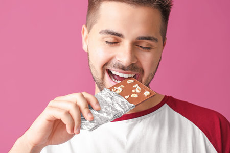 Handsome young man with tasty chocolate on color backgroundの写真素材
