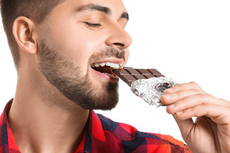 Handsome young man with tasty chocolate on white backgroundの写真素材