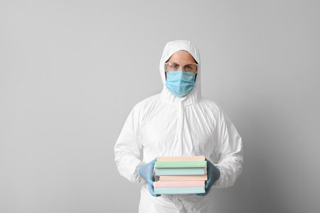 Man in biohazard suit and with books on gray backgroundの写真素材