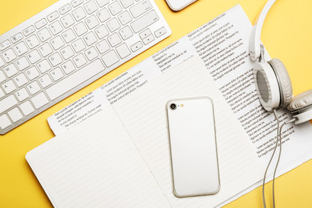 Computer keyboard with mobile phone, headphones, notebook and newspaper on color backgroundの写真素材