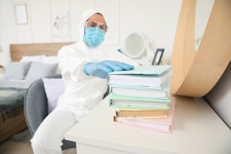 Man in biohazard suit and with books at homeの写真素材