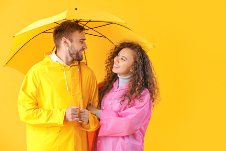 Happy young couple with umbrella on color backgroundの写真素材