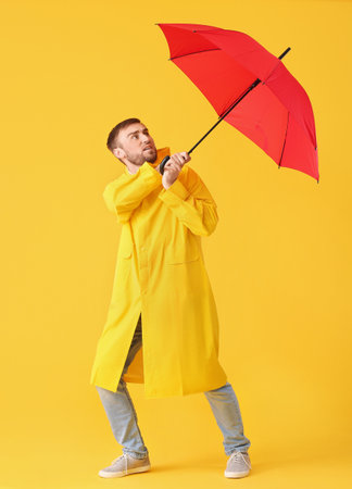 Handsome young man with umbrella on color backgroundの写真素材