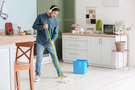 Handsome young man mopping floor in kitchenの写真素材