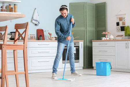 Handsome young man mopping floor in kitchenの写真素材