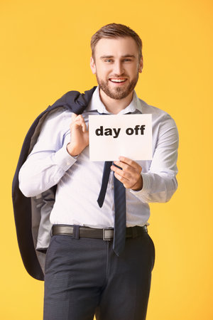 Young businessman holding paper with text DAY OFF against color backgroundの写真素材