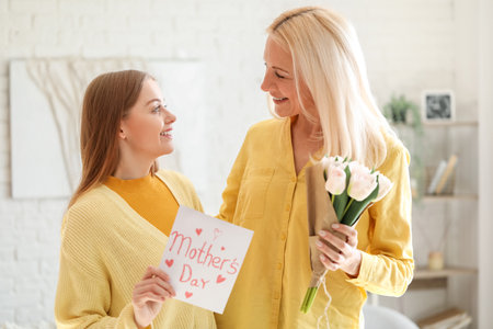 Young woman greeting her mother with tulips and card at homeの写真素材