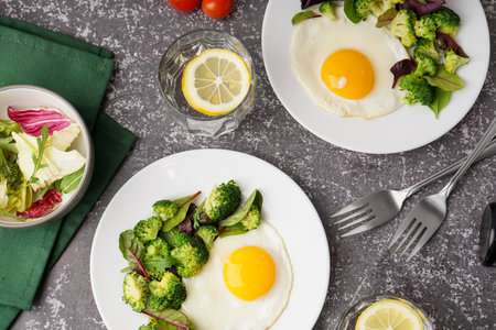 Plates with tasty fried eggs, broccoli and spinach on gray grunge backgroundの写真素材