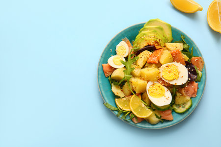 Plate of tasty potato salad with eggs and avocado on light blue background, top viewの写真素材