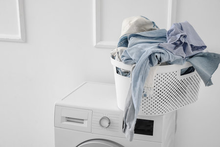 Laundry basket with dirty clothes on washing machine near light wallの写真素材