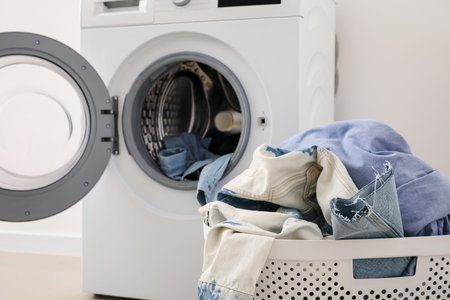 Laundry basket with dirty clothes and washing machine near light wall in roomの写真素材