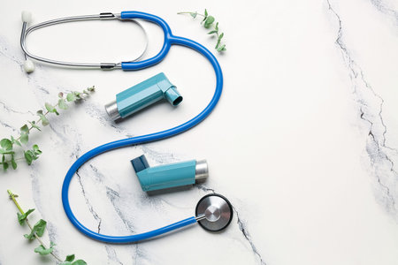 Asthma inhalers with stethoscope and eucalyptus branches on grunge background