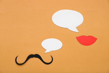 Paper mustache and lips with speech bubbles on orange background. Dialogue conceptの写真素材