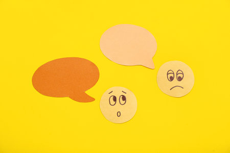 Paper faces with speech bubbles on yellow background. Dialogue conceptの写真素材