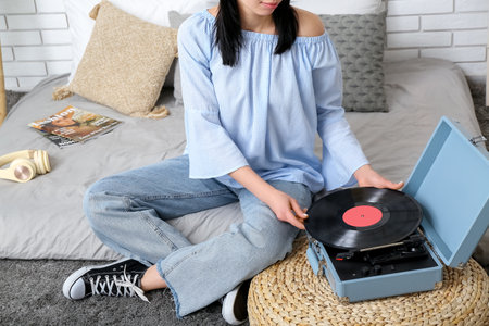 Young woman with record player in bedroomの写真素材