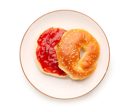 Plate of tasty bagel with strawberry jam on white backgroundの写真素材