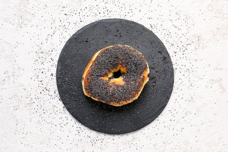 Slate board of tasty bagel with poppy seeds on light backgroundの写真素材