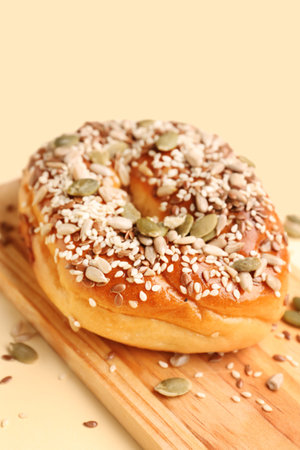 Wooden board of tasty bagel with sesame and pumpkin seeds on beige background, closeupの写真素材