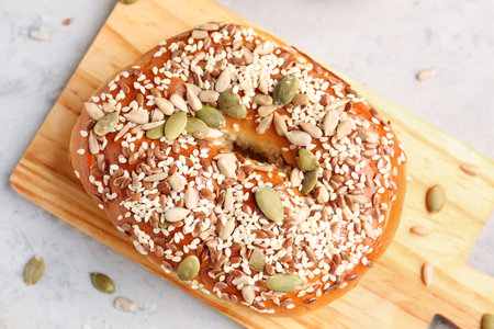 Wooden board of tasty bagel with sesame and pumpkin seeds on grunge background, closeup