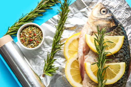 Aluminum foil roll with fresh raw fish, lemon slices, rosemary and spices on color background, closeupの写真素材