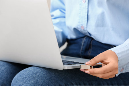 Woman using USB flash drive with modern laptop, closeup