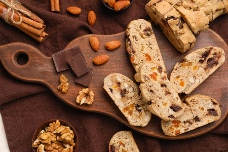 Wooden board with tasty biscotti cookies, chocolate, nuts and cinnamon on fabric background, closeupの写真素材