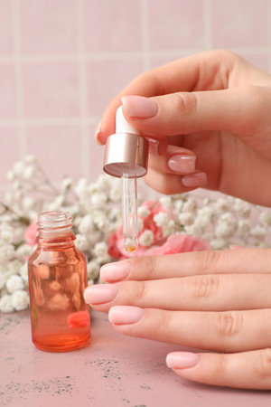 Female hands with bottle of cuticle oil and flowers near color tile background, closeupの写真素材